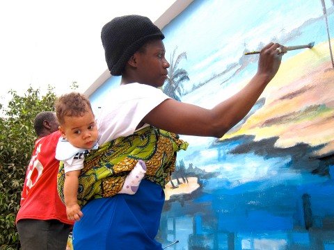 20 augustus 2012 › Sous les encouragements de son fils Quentin, Rhode Makoumbou réalise la fresque «Le village de pêcheurs».