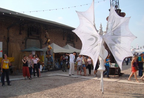 28 juin 2009 › Parade d'une danseuse sur échasses au Festival Couleur Café. En arrière-plan : la sculpture «La porteuse d'eau».